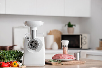 Modern meat grinder with vegetables and beef on table in kitchen