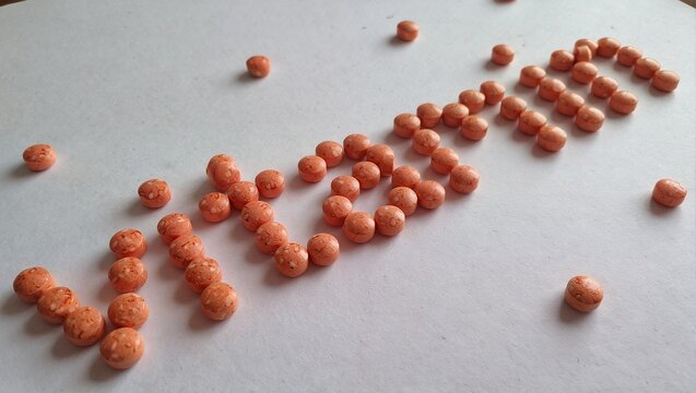 a scattering of small, orange, spherical candies arranged to spell out the word "vitamin" on a white surface.