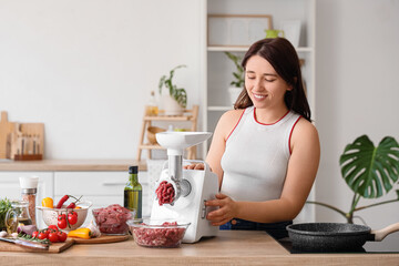 Young woman using meat grinder at table in kitchen