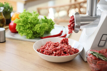 Meat grinder with minced beef and vegetables on table in kitchen, closeup