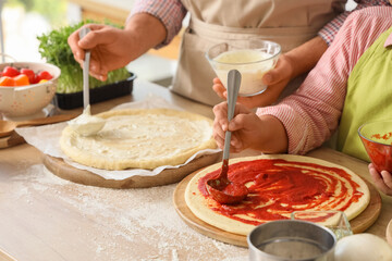 Father with his little daughter applying sauces on pizza dough in kitchen, closeup