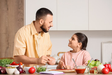 Little girl with her father putting sausage on pizza dough at table in kitchen