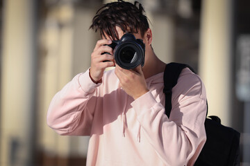 Young happy male photographer with camera and backpack taking photo on street