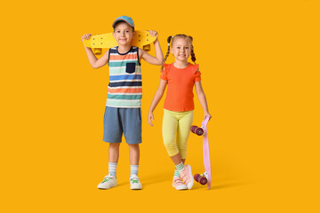 Stylish little children with skateboards on yellow background