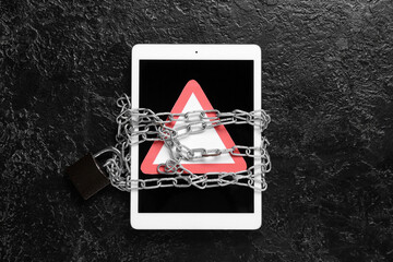 Tablet computer with warning sign and chains on dark background. Crime concept