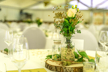 Eine helle, große Festzelt-Location ist für eine Feier festlich eingedeckt, wobei runde Tische...