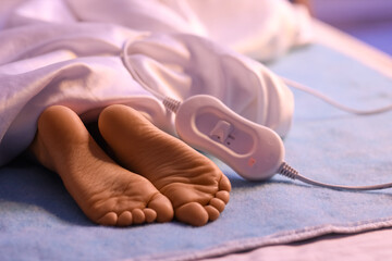 Little girl's feet lying under blanket on electric heating pad in bedroom at night, closeup