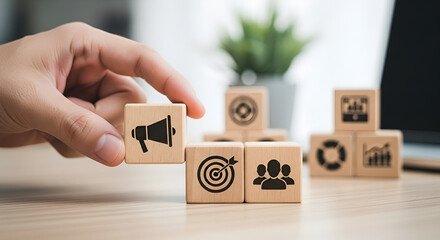 Hand arranging wooden blocks with marketing strategy icons for business growth, a concept of goal setting, advertising, and audience targeting