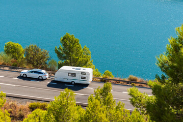 Car with caravan on a seaside road surrounded by trees and ocean views