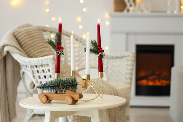 Burning candles with Christmas branches and toys on table in living room