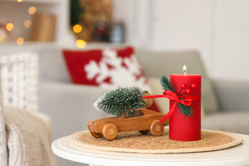 Burning candle with Christmas tree and toy car on table in living room, closeup