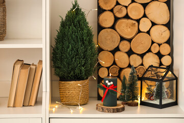Burning candle with Christmas trees on shelf in living room