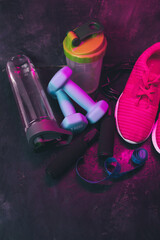 Neon-lit fitness gear on dark textured background, pink sneakers, dumbbells, jump rope, shaker, water bottle and measuring tape in cyberpunk workout style