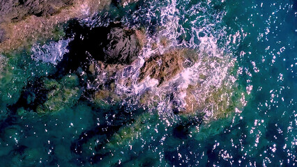 Waves Crashing Over Rocks in Clear Blue Water During Sunlight on a Coastal Shore