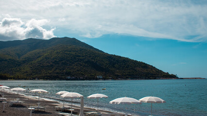 Sunshine Reflects off the Calm Sea With White Umbrellas Lining the Sandy Beach Near a Green Mountain in Summer. Sapri, Campania, Italy