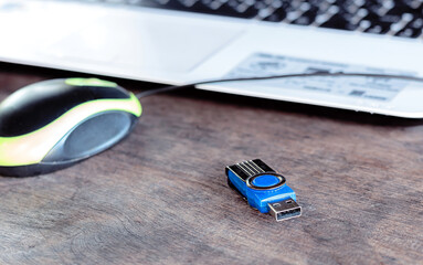 Close-up of USB flash drive, mouse, and laptop keyboard on wooden desk—everyday tech tools in a casual workspace.