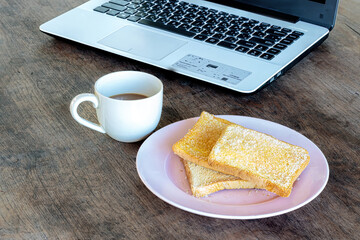 Coffee, toast, and laptop on wooden table—casual morning setup blending comfort food with a relaxed work atmosphere.