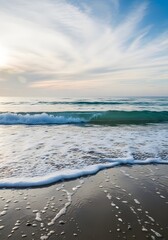 Ocean waves gently rolling onto the shore under a bright and cloudy sky at sunrise