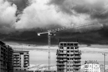 Dźwig wieżowy oraz osiedle wysokich budynk&oacute;w mieszkalnych w budowie. Pochmurne niebo. 