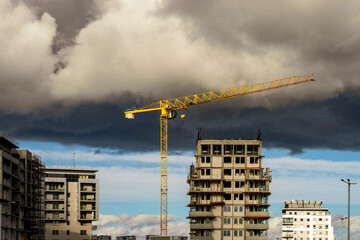 Dźwig wieżowy oraz osiedle wysokich budynk&oacute;w mieszkalnych w budowie. Pochmurne niebo. 