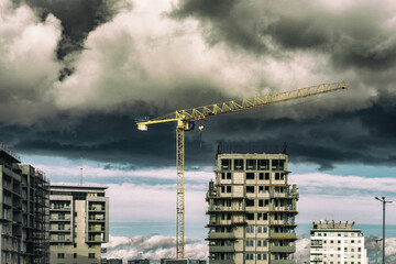 Dźwig wieżowy oraz osiedle wysokich budynk&oacute;w mieszkalnych w budowie. Pochmurne niebo. 