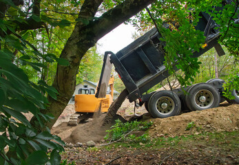 A dump truck dumping a load of sand into an excavation for a home septic system waste field