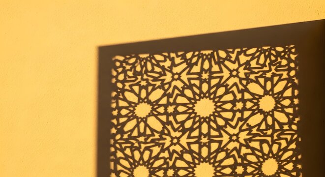 Geometric Islamic pattern shadow cast on a textured yellow wall at golden hour
