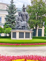 Obraz premium Kazan Kremlin,Kazan,Russia,July 26,2024: Kul Sharif.A bronze statue of two symbolic medieval builders with architectural plans,set in a green garden surrounded by flowers and historic buildings.