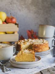A slice of apple pie served alongside coffee, cake, and a box of organic apples in the background.
