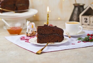 Sliced ​​homemade Sachertorte made of two chocolate layers, layered with apricot jam and covered with chocolate icing on a white plate in a Christmas theme.