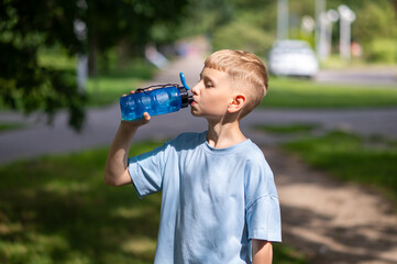 Teenage boy drinking water from sports bottle outdoors on a warm sunny day