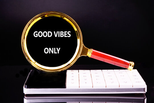 A golden magnifying glass rests on a calculator. The glass displays the words Good Vibes Only against a black background, emphasizing a positive outlook at work or in studies