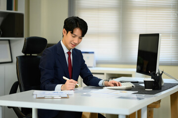 Professional banker reviewing business charts, writing notes, and calculating figures in a modern office