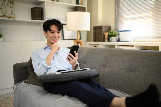 A relaxed man smiles while checking his smartphone during a remote work session, balancing productivity and connection