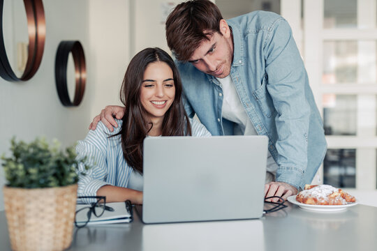 A young couple enjoys a morning at home, smiling while working together on a laptop. The warm light and teamwork reflect love, productivity, and a modern lifestyle balance.