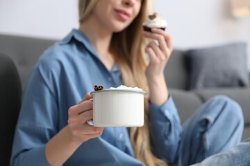 Fototapeta premium Woman enjoying tasty cocoa drink and cupcake at home, closeup