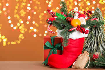 Saint Nicholas day. Red boot with treats and festive decor on table against blurred lights. Space for text