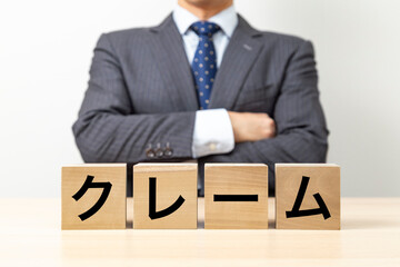 「クレーム」と書かれたブロックと腕組みをするビジネスマン
