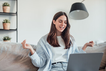 Smiling girl sit on couch at home wave talk with friend or family having video call on laptop,...