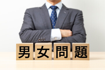 Obraz premium 「男女問題」と書かれたブロックと腕組みをするビジネスマン