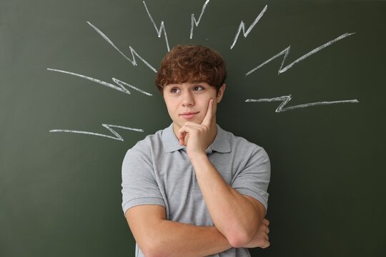 Back to school. Thoughtful boy near chalkboard with drawn lightning bolts indoors