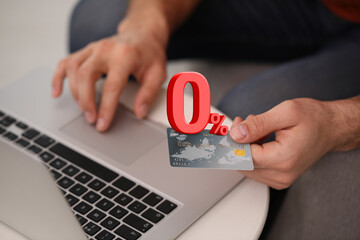Man with credit card using laptop at table, closeup. 0 percent sign for zero commission