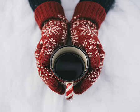 Cozy hands in festive mittens holding warm mug of coffee amidst winter snow, perfect for holiday cheer - Powered by Adobe