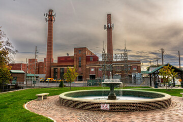 small fountain bench and brick walkway with large brick power plant and very tall smoke stacks in background