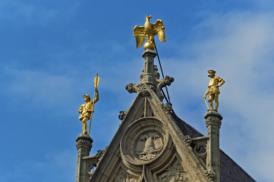  a golden eagle with wings partially spread. Flanking the pediment are two golden statues atop columns &mdash; one holding a staff, the other a sword in Antwerp