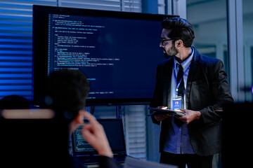 A focused male AI solutions architect in a futuristic control hub debates generative AI applications collaborating on a complex machine learning model with his team under atmospheric blue lighting.
