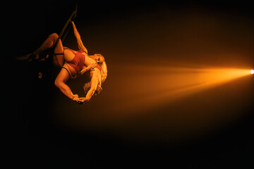 Female aerialist on hoop (lyra) in an elegant backbend under warm golden spotlight—strength and flexibility  horizontal with wide right-side negative space. © Dima