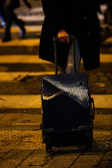 A traveler with luggage on a city street at night.