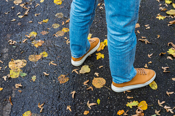 High-angle shot of legs in trendy denim and modern brown leather sneakers, paused on a dark paved...