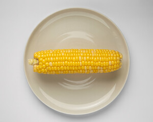 Freshly harvested golden corn cob artfully presented on a minimalist plate, capturing natural sweetness and healthy eating appeal.